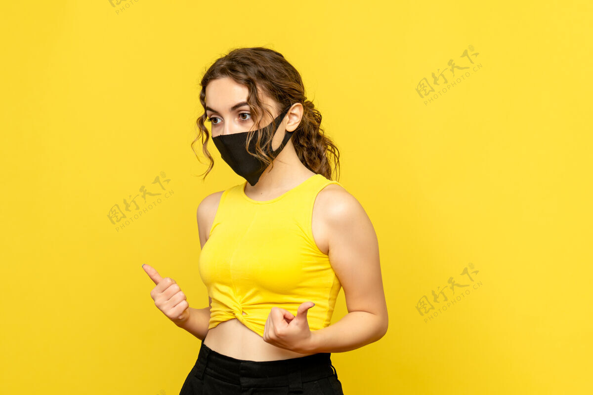 时尚黄色墙上戴着面具的年轻女子的正视图年轻人人模特
