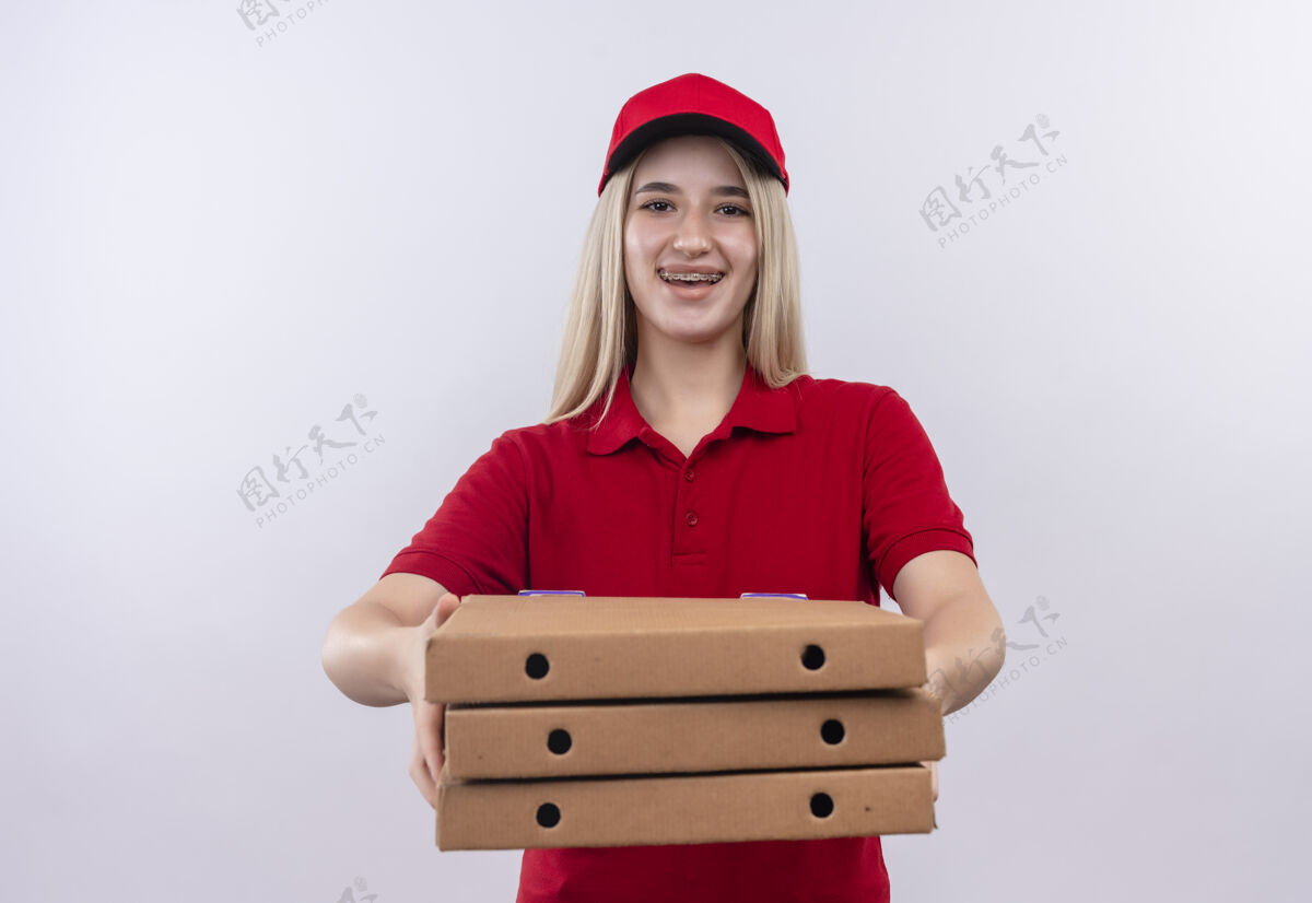 牙科微笑的小女孩穿着红色t恤 戴着帽子 戴着牙套 在孤立的白色背景下拿着比萨饼盒对着镜头支撑盒子年轻