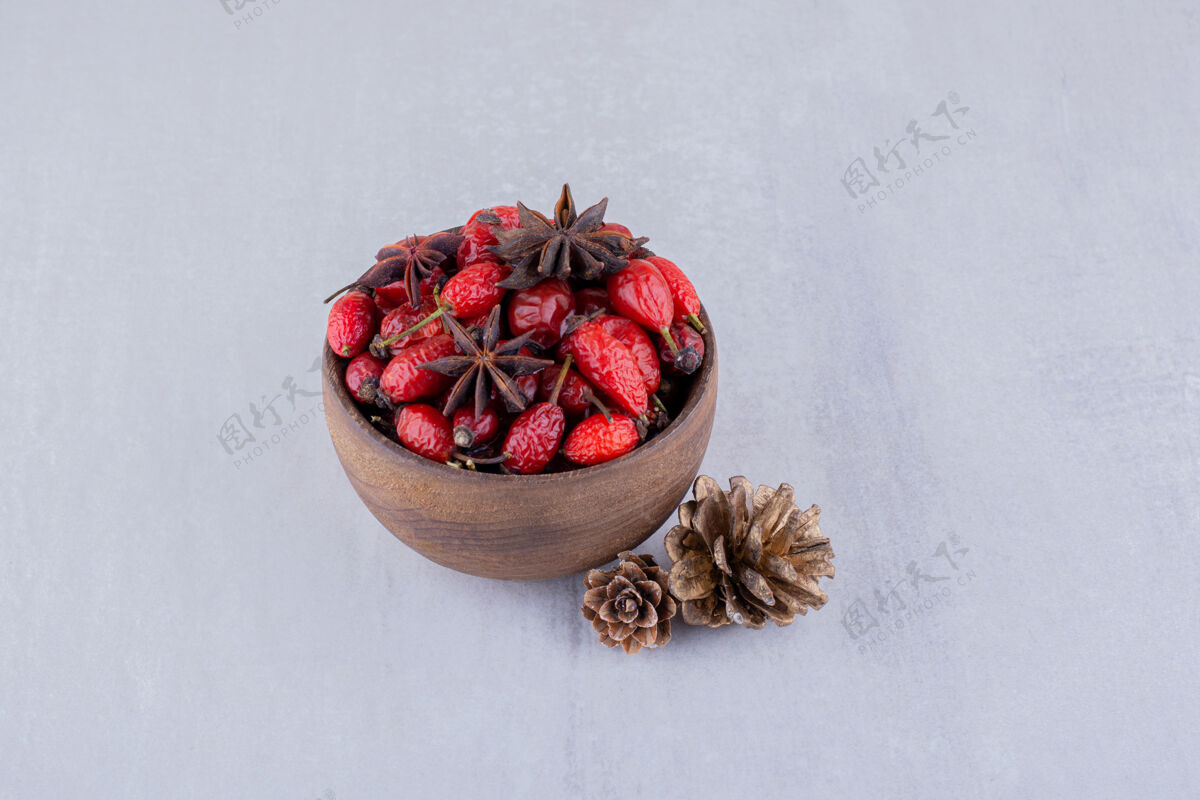 茶两个松果旁边的木碗臀部和茴香白色背景松果冲泡玫瑰