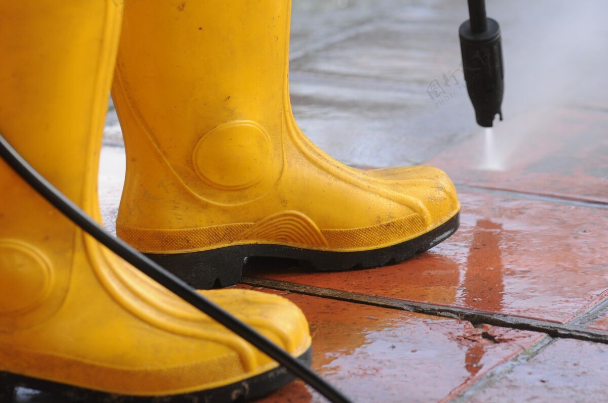 清洗穿黄色胶靴的人用高压水嘴清洗瓷砖上的污垢喷雾清洗橡胶