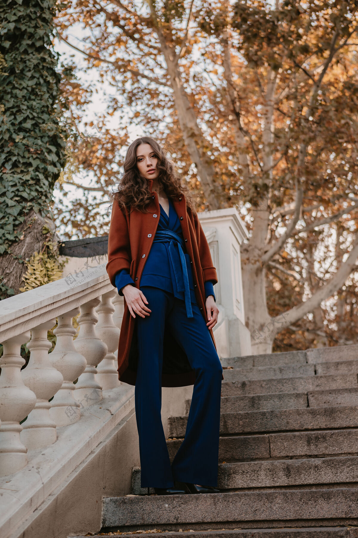 魅力美丽时尚的微笑瘦身女子卷发走在街头楼梯上穿着温暖的棕色外套和蓝色西装 秋季时尚街头风套装时尚优雅