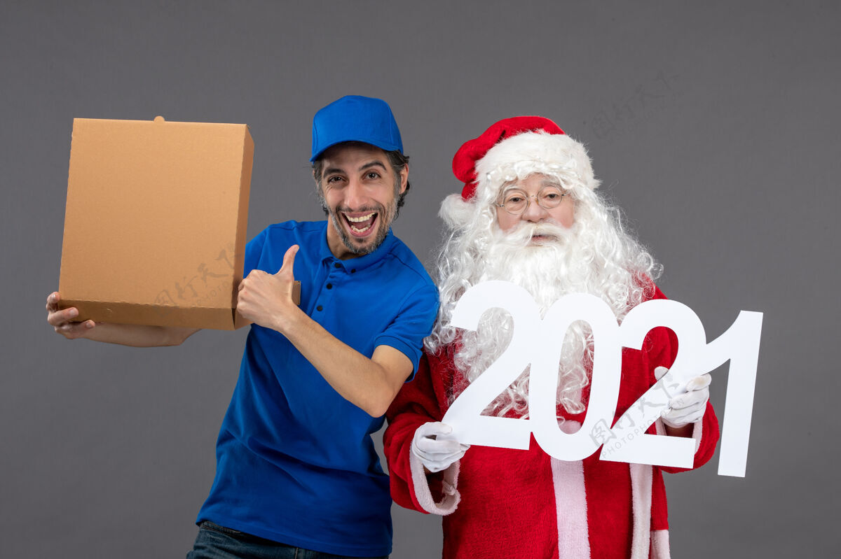 举行圣诞老人的正面图 男信使拿着食物盒 站在灰色的墙上节日人盒子