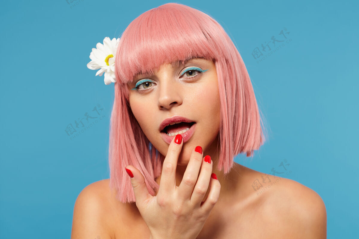 砰砰摄影棚的照片 年轻可爱的粉红色头发的女士与彩妆举行食指对她的内衣 而看着相机与平静的脸 站在蓝色的背景下色彩洋甘菊肩部