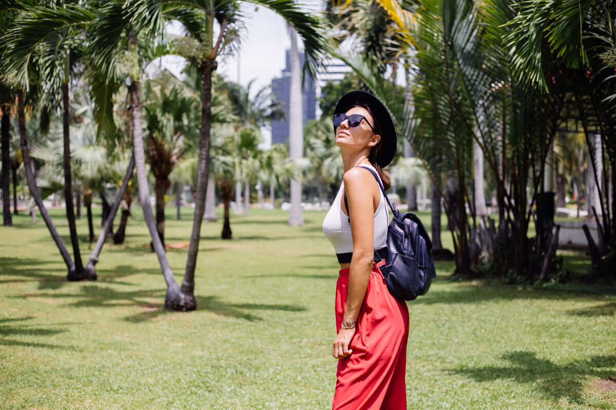 平静快乐女人背着背包环游曼谷 在绿草如茵的热带公园里享受美丽的晴天自然热带草地