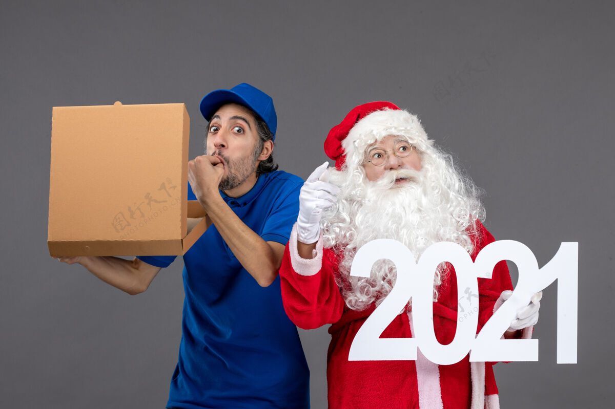 人圣诞老人的正面图 灰色的墙上有男信使拿着购物袋和食品盒男举行信使