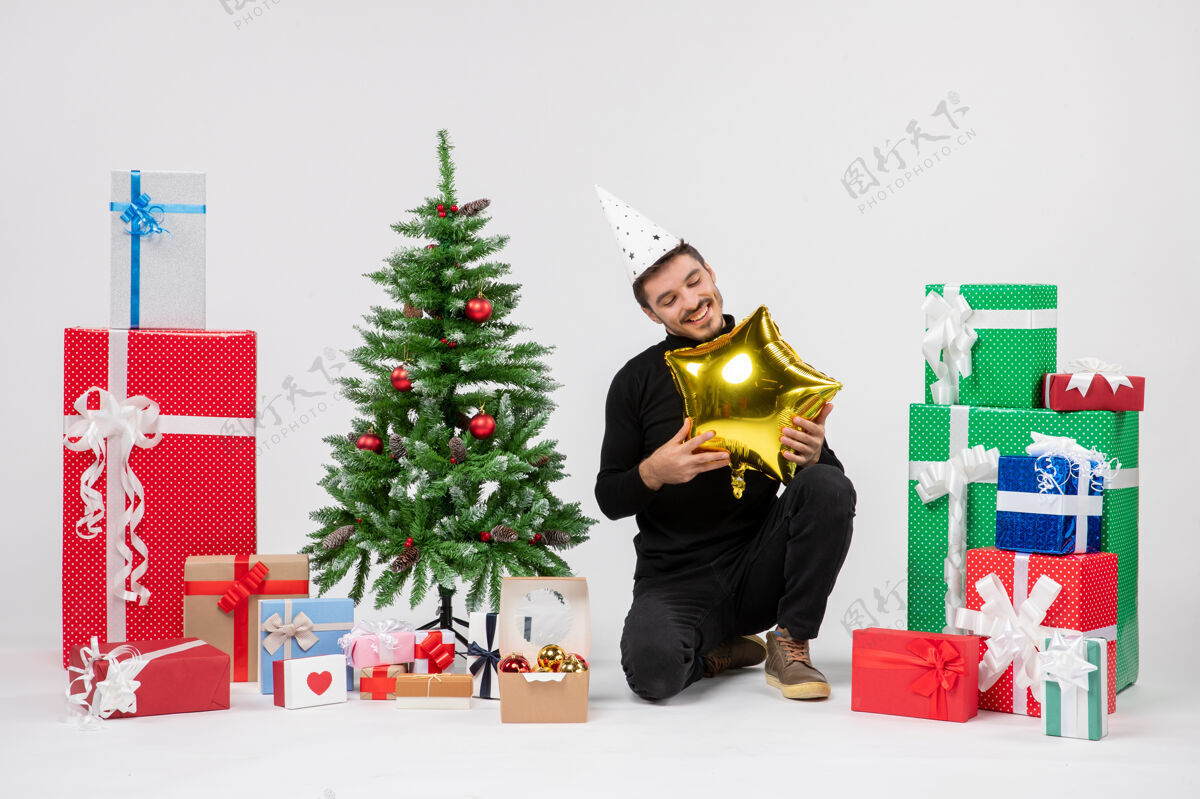 节日正面图：年轻人围坐在礼物旁边 手里拿着白色墙上的金星形气球抱着黄金十二月