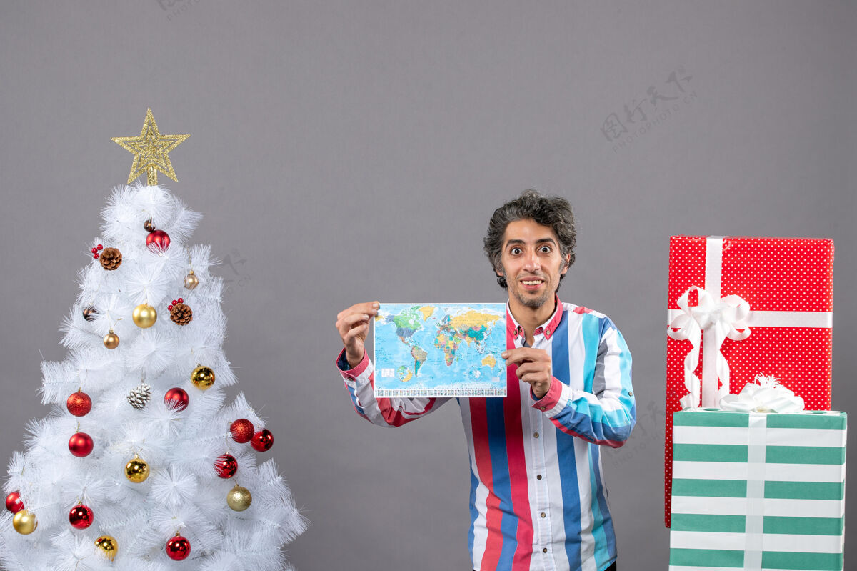 假期正面图微笑的男人穿着条纹衬衫拿着白色圣诞树附近的地图 并提供复印空间圣诞树微笑搞笑