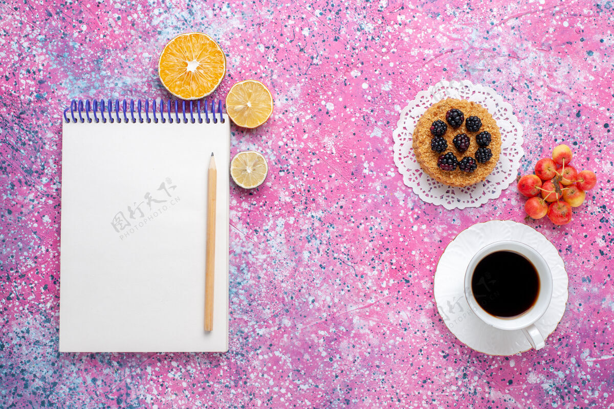 水果顶视图一杯茶 粉红色背景上有小蛋糕和记事本烘焙五颜六色顶部