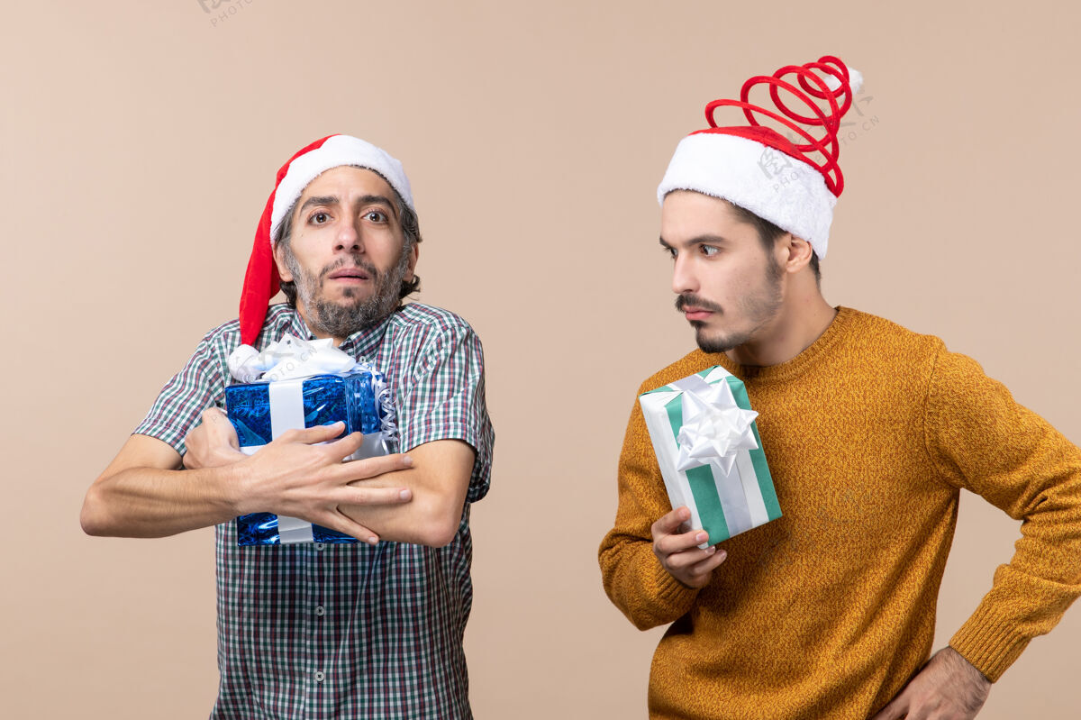 视图正面图两个戴着圣诞帽的窥探者拿着他们的礼物 背景是米色的前面微笑戴着