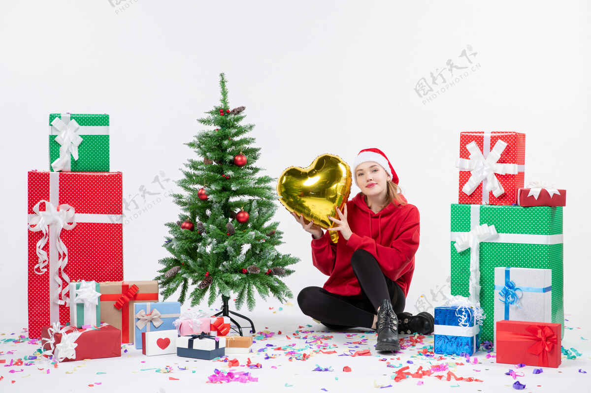 礼物前视图年轻女子围坐在一个白色的墙上拿着金色的心形礼物坐着冬天树