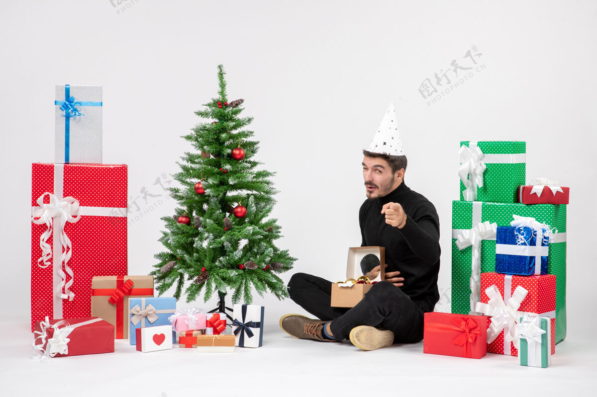 情绪年轻人坐在白色墙上的节日礼物周围的正面视图十二月圣诞节日