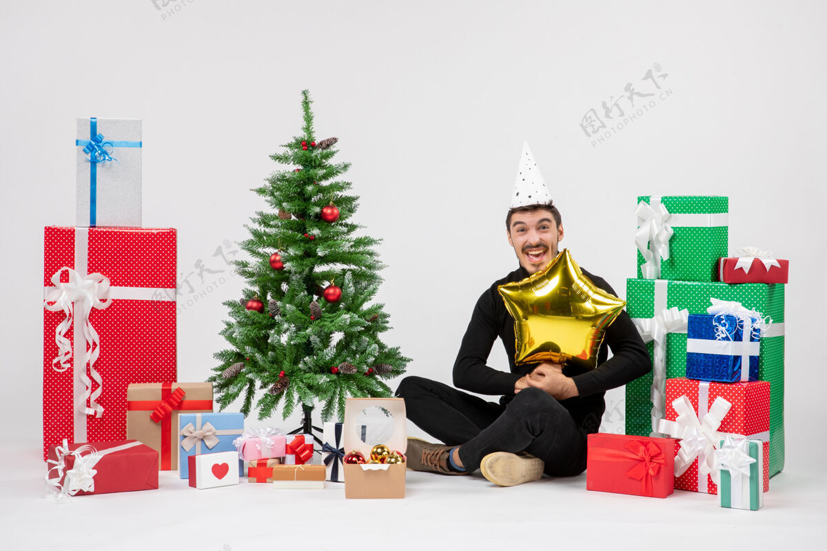庆祝正面图：年轻人围坐在礼物旁边 手里拿着白色墙上的金星人装饰圣诞树