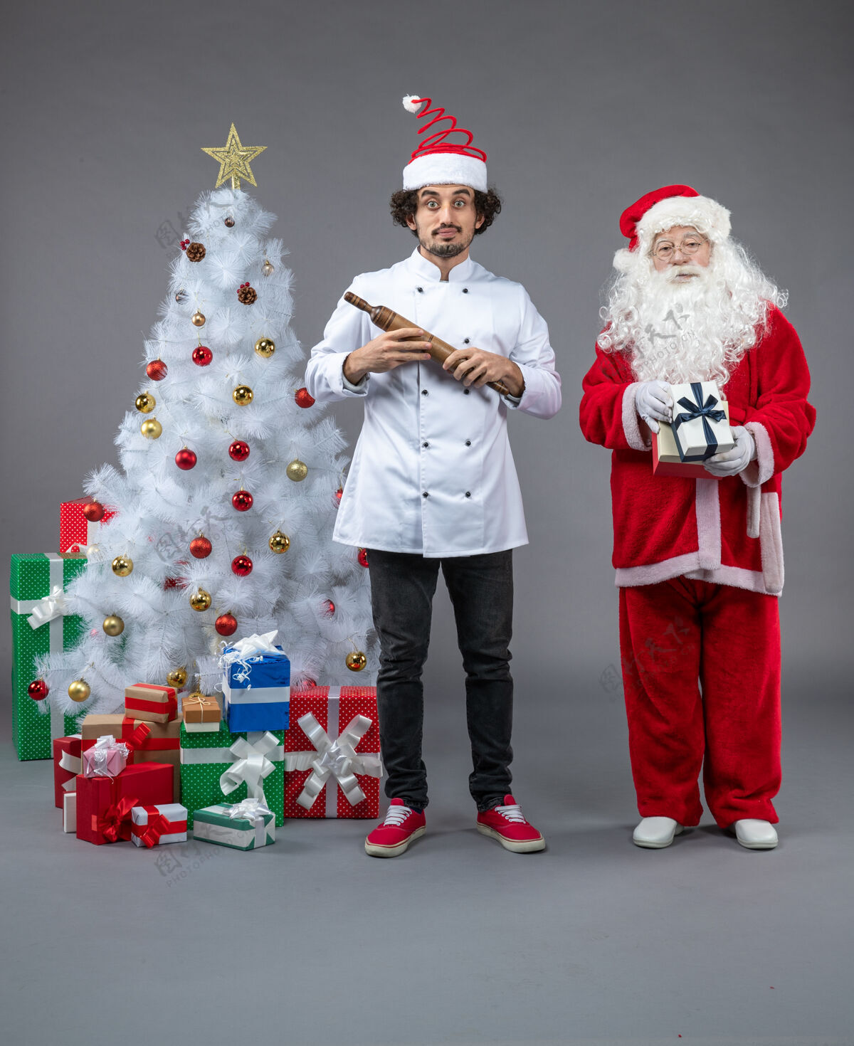 人们圣诞老人和男厨师在灰色墙上围着圣诞礼物的正视图快乐男性帽子