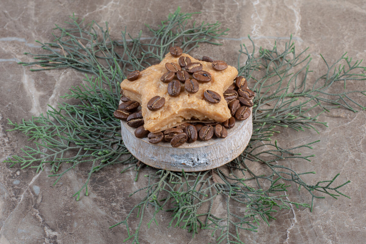 甜点星星形状的饼干放在一堆咖啡豆上 放在大理石的小底座上树叶可口美味