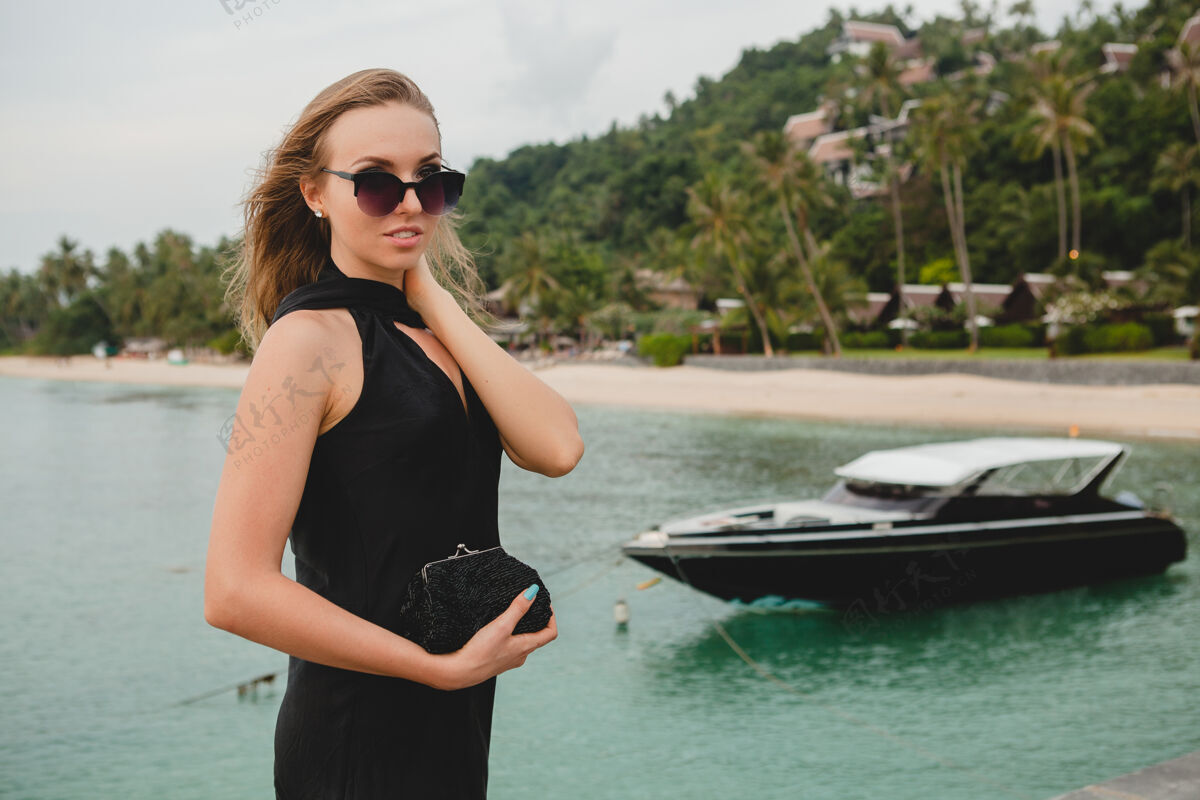 女士奢华性感迷人的女人穿着黑色礼服在豪华度假酒店的码头上摆造型 戴着墨镜 暑假 热带海滩优雅邮轮天堂