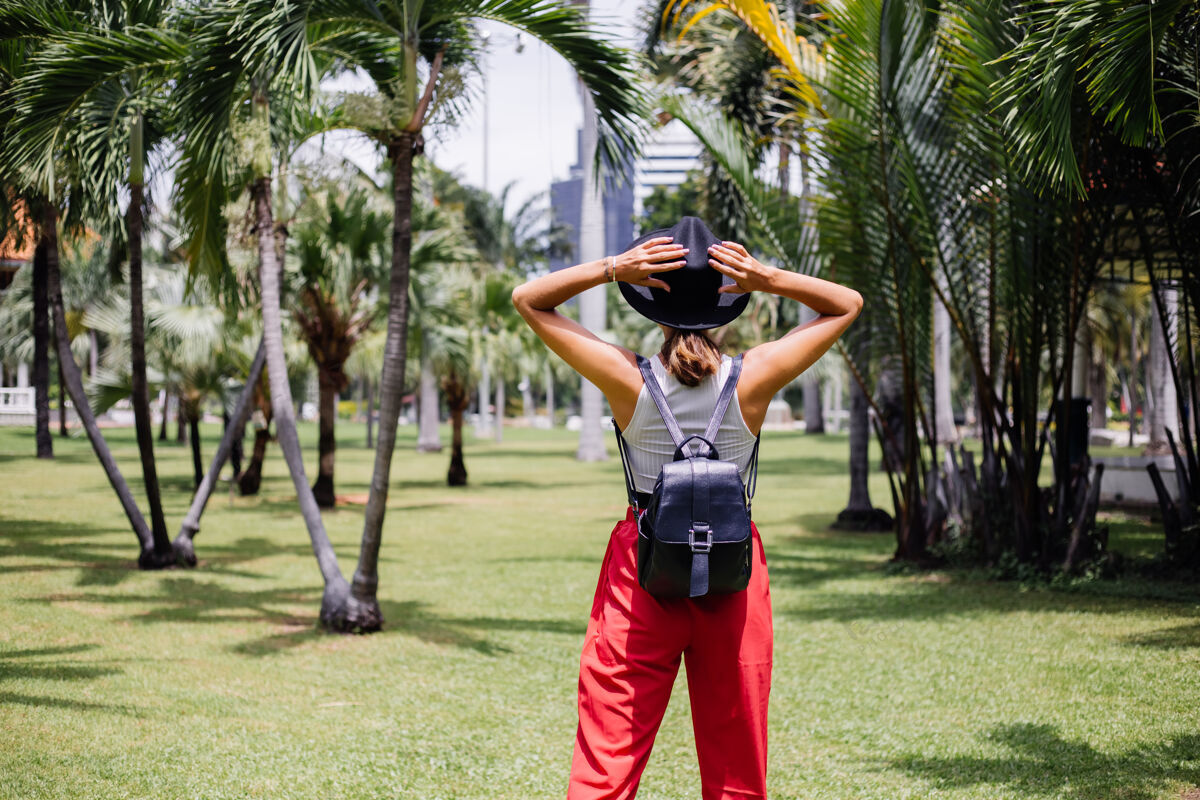 热带快乐女人背着背包环游曼谷 在绿草如茵的热带公园里享受美丽的晴天热带棕榈景观