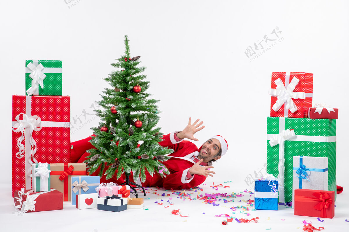 圣诞节日气氛与年轻的圣诞老人躺在圣诞树后靠近礼物白色背景圣诞老人季节年轻