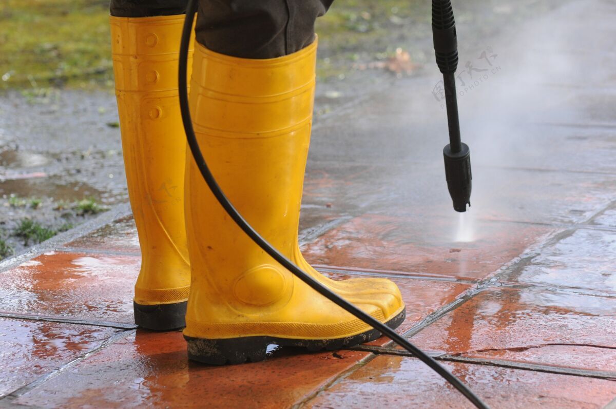 物体穿黄色胶靴的人用高压水嘴清洗瓷砖上的污垢水清洁污垢