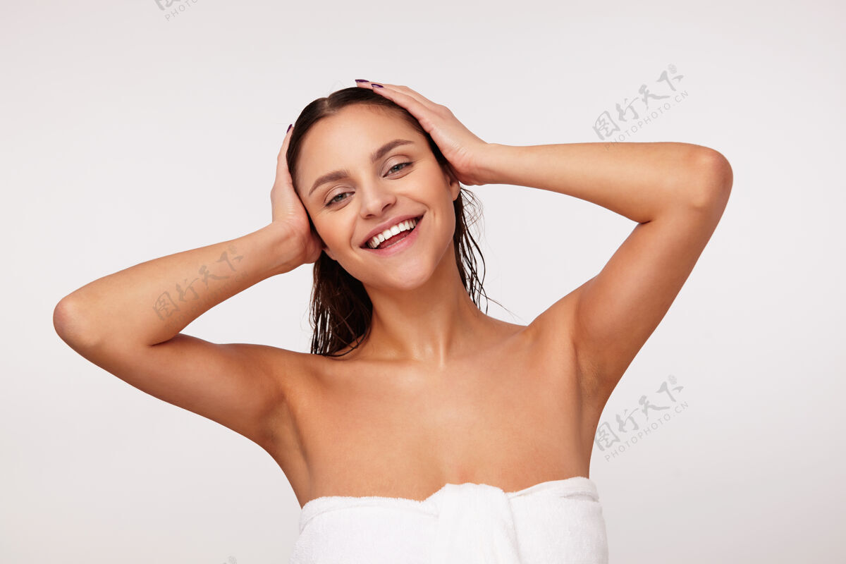 抬高可爱的年轻漂亮的碧眼黑发女子 双手握在湿漉漉的头上 真诚地微笑着 沐浴后摆出姿势护理淋浴洗澡