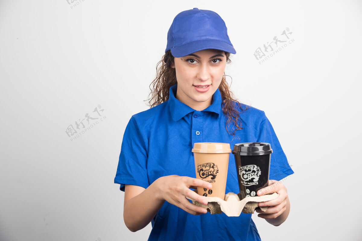 黑发穿着蓝色制服的女人拿着两杯咖啡 背景是白色的高质量的照片帽子马克杯年轻人
