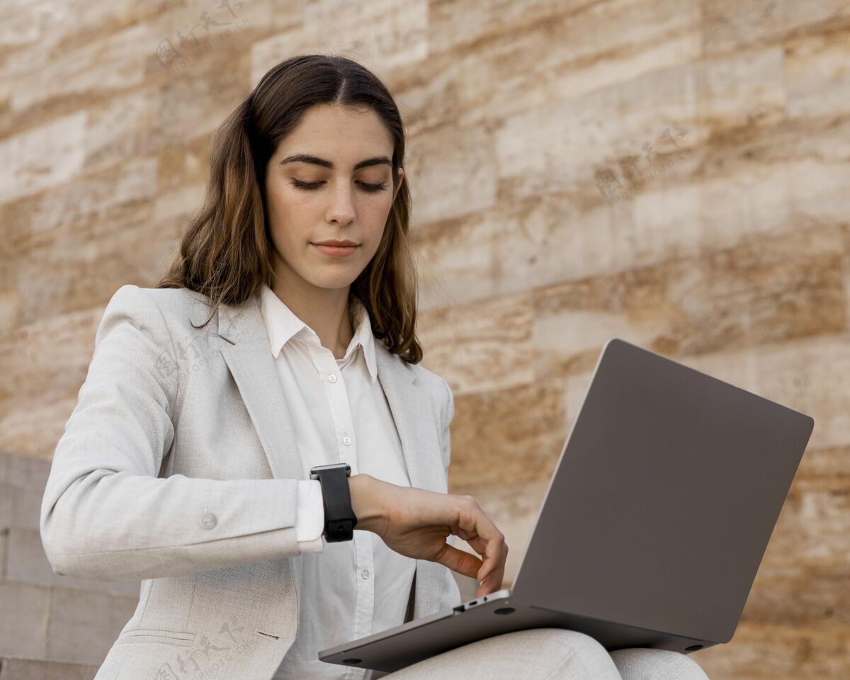 个人优雅的女商人在户外看着智能手表和笔记本电脑企业家个人复杂
