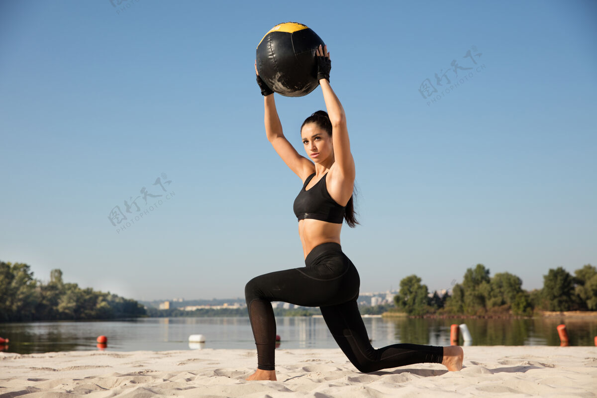 健康年轻健康的女子在沙滩上带球做弓箭步海滩成年人女人