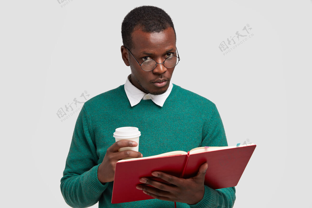 美国严肃的深色皮肤的男书生留着短发 拿着课本 拿出咖啡个人个性教科书