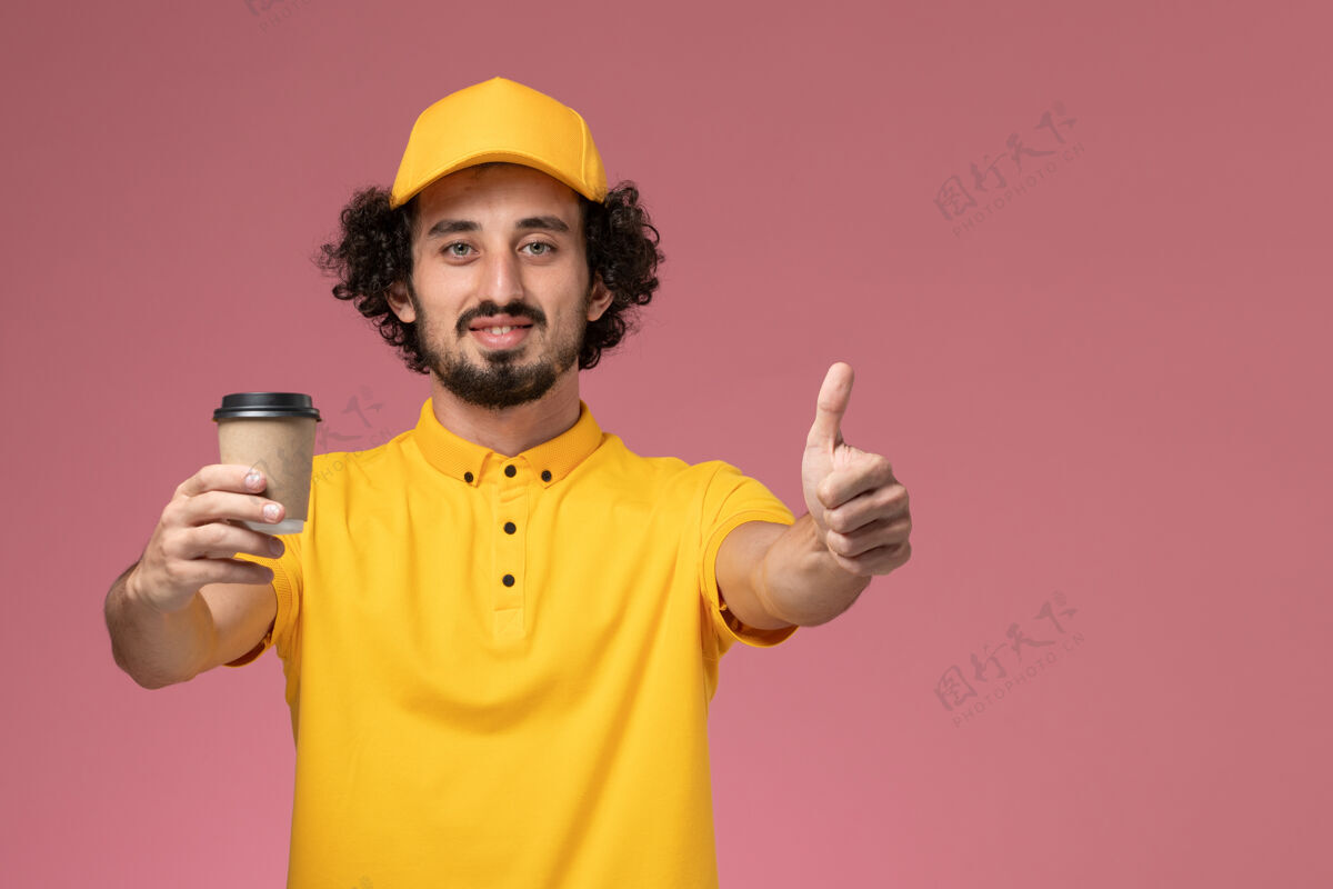 视野正面图：身穿黄色制服 披风的男性快递员在粉色墙上拿着送货咖啡杯制服工作服务
