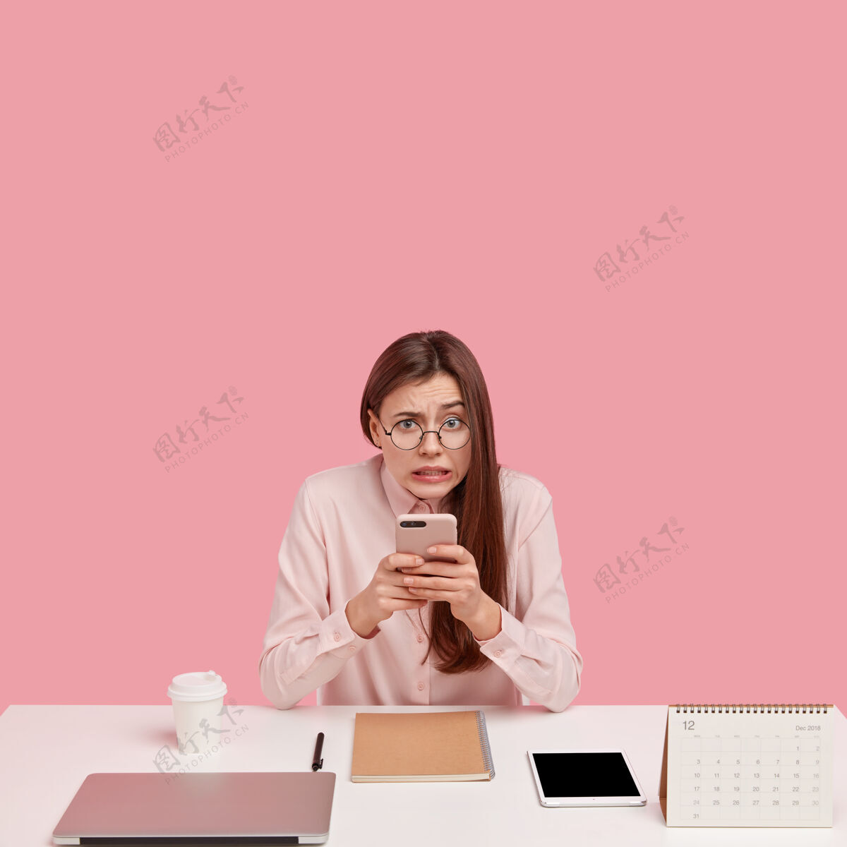 人类失意女子的照片手持手机 通过在线bannking应用程序汇款 周围有笔记本电脑 螺旋记事本 日历日历工作青少年