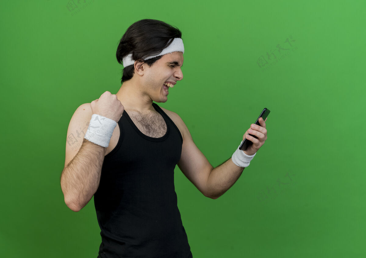 看穿着运动服 头戴头巾的年轻人看着自己的智能手机屏幕握紧拳头高兴又兴奋绿色男人头带