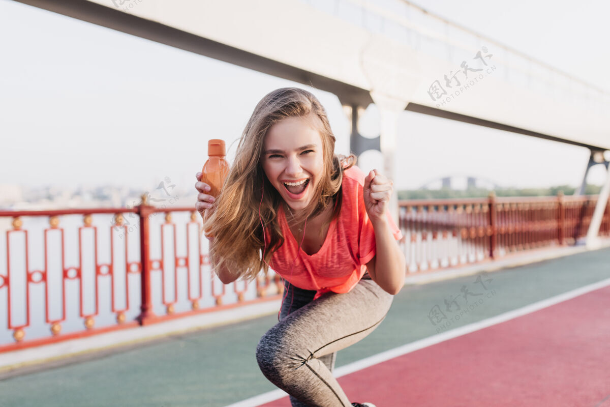 时尚欣喜若狂的白人女孩在夏季马拉松比赛中玩得很开心户外肖像灵感女模特在体育场摆出快乐的微笑跑步比赛轨道