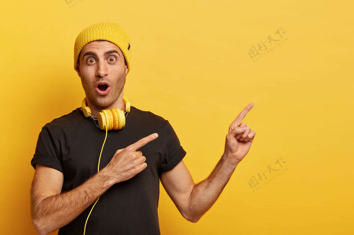 惊讶音乐是科技的一部分惊讶的白种人戴着耳机 戴着黄色的头饰和黑色的t恤手音乐广告