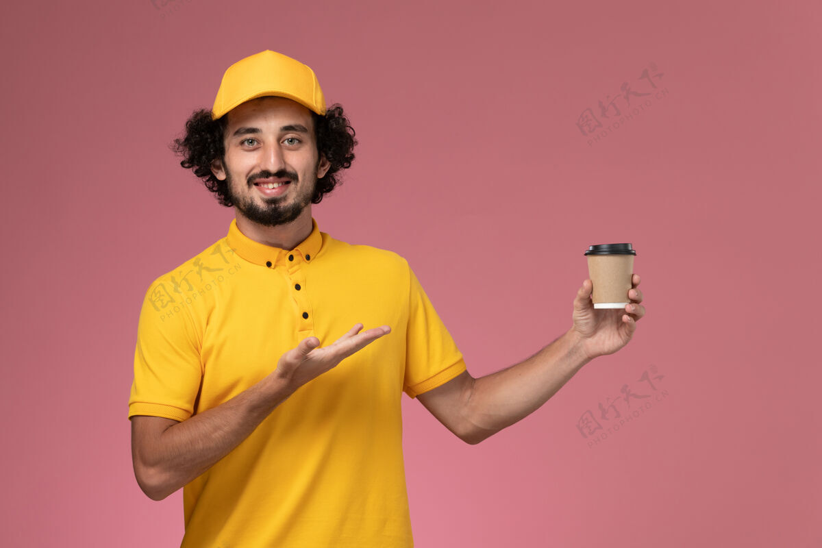 粉色正面图：身穿黄色制服 披风的男性快递员在粉色墙上拿着送货咖啡杯工作正面送货