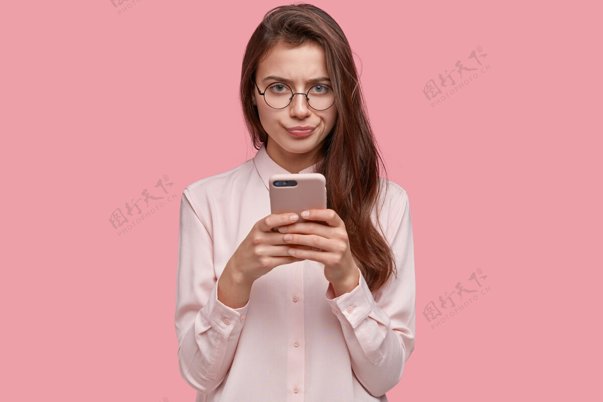 智能手机严肃的女朋友形象和不悦的表情 按嘴唇 携带现代手机 在社交网络中交流保持信息惊喜