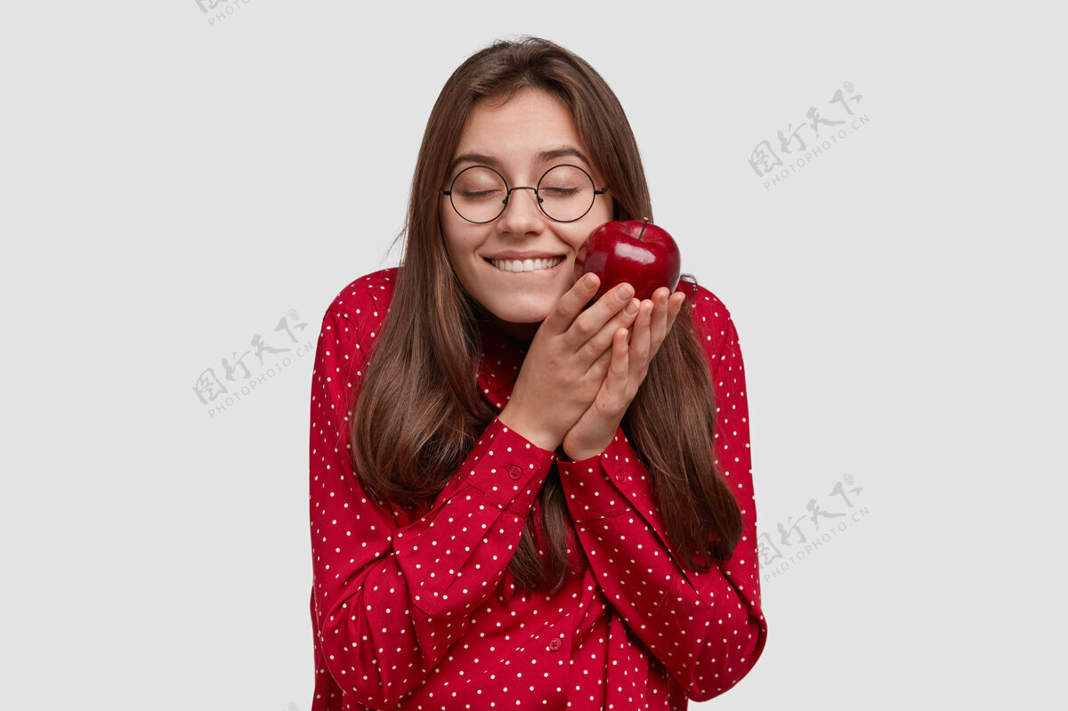 节食喜极而泣的黑发女人心情愉悦 捧着美味的苹果 精神抖擞 穿着红衣服凝视服装满意