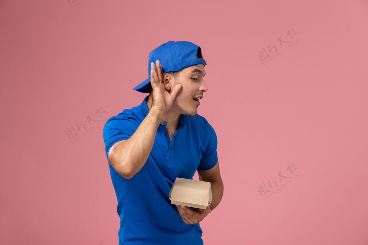 送货正面图：身穿蓝色制服披肩的年轻男性快递员手持粉色墙上的快递食品包人员工快递