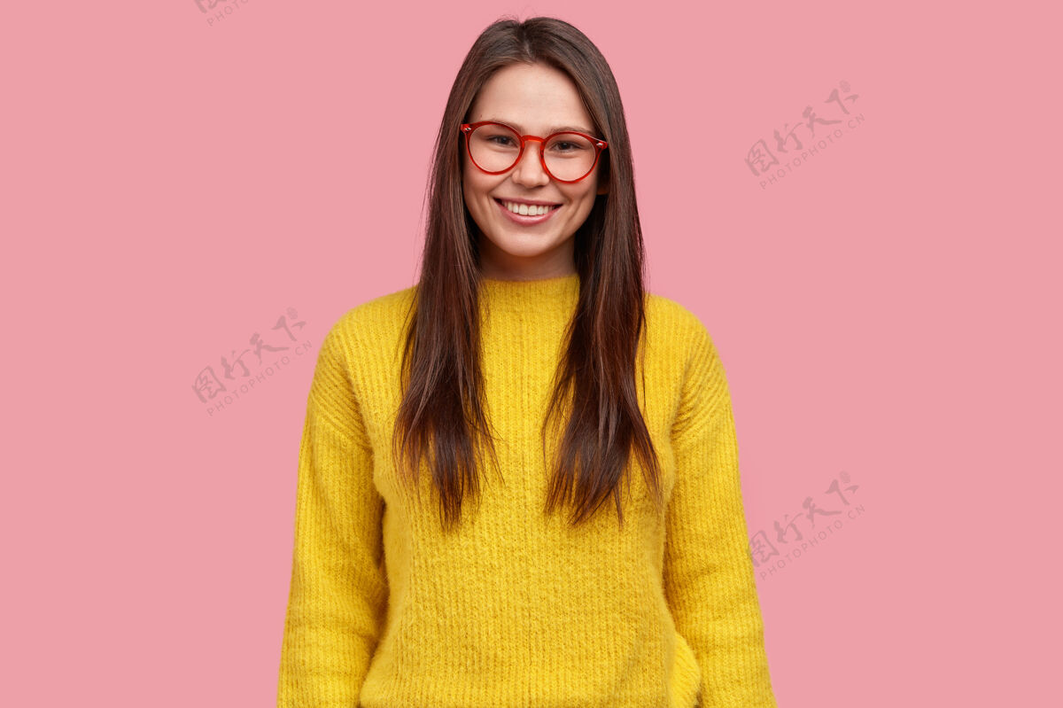 工作满意的漂亮黑发年轻女子的上身镜头 表情愉快 戴着眼镜和黄色休闲套头衫 粉色背景下的模特成功满意眼镜