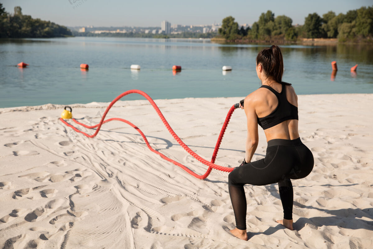运动年轻健康的女人在沙滩上用绳子做运动运动员身体健美运动员