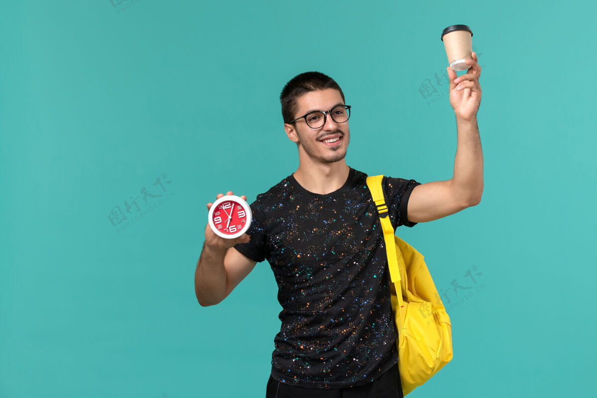 哑铃身穿深色t恤的男生正面图黄色背包 蓝色墙上挂着咖啡和时钟体重学生书籍