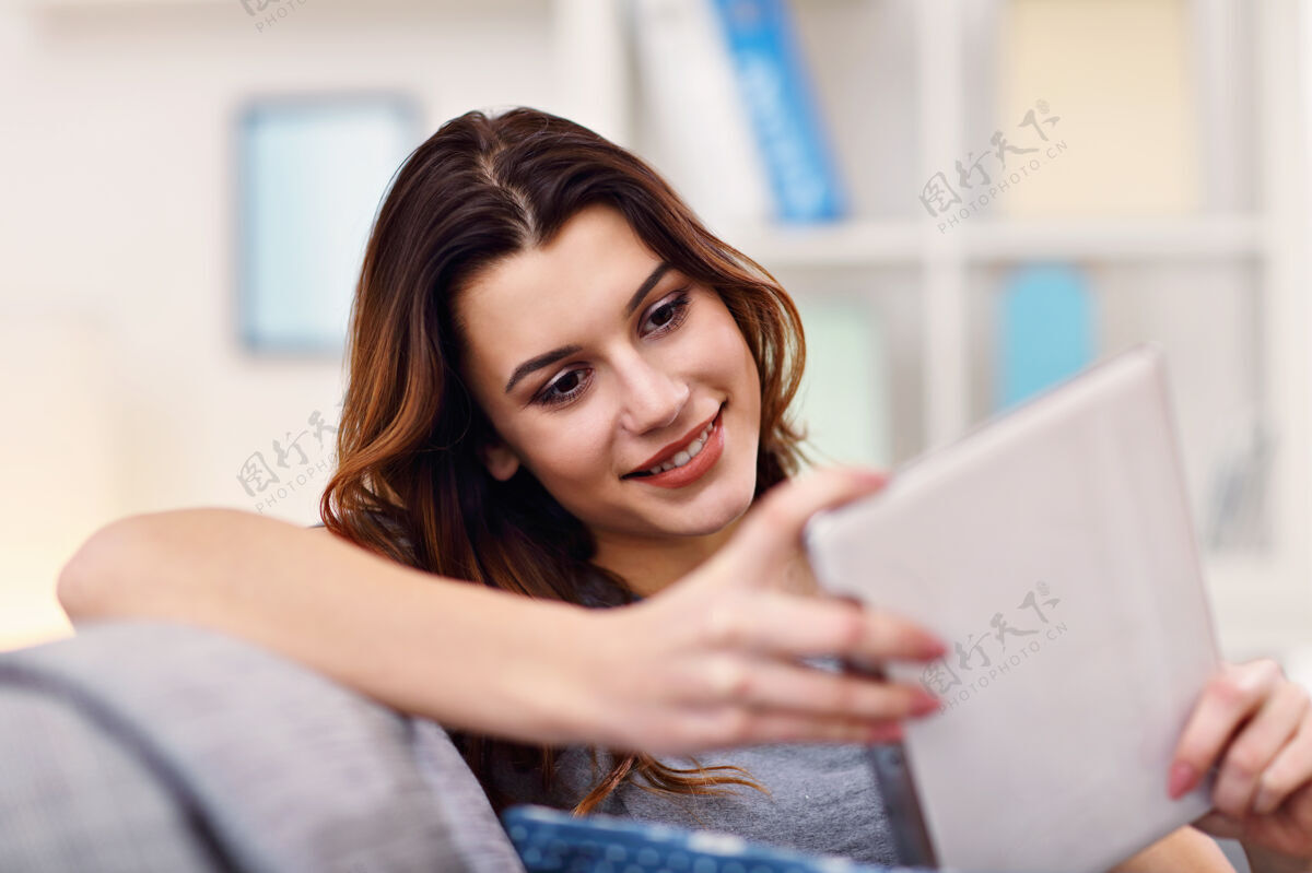 女性快乐的成年女人在家里客厅里用电话社交媒体信息平板电脑