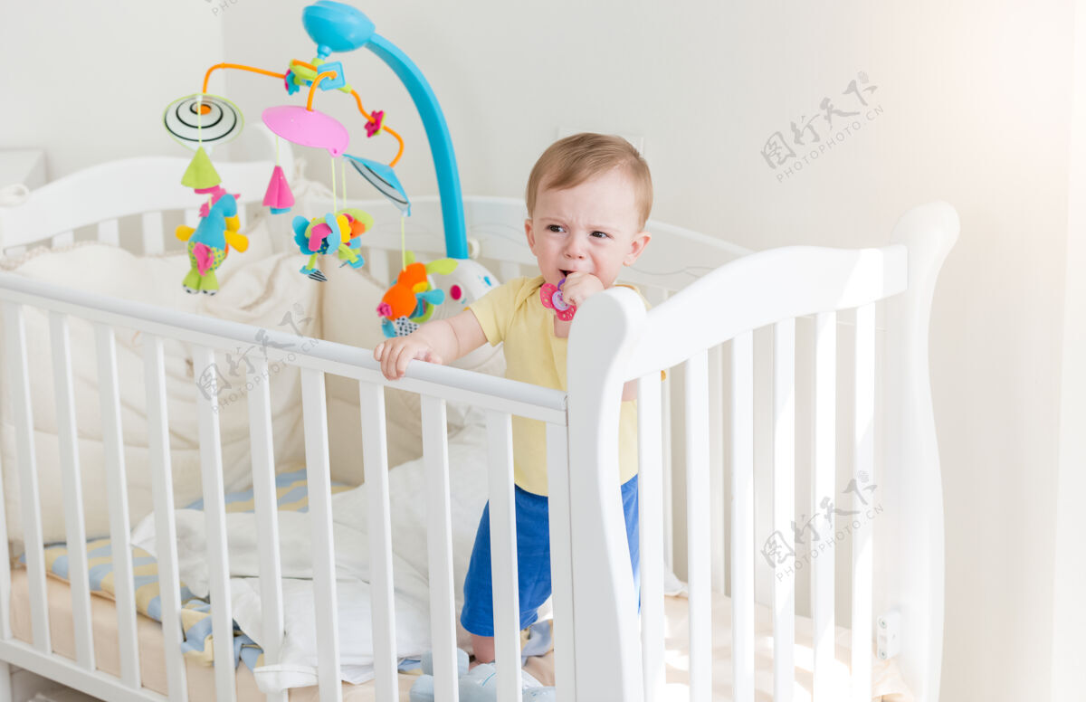 卧室伤心的10个月大的男婴哭着抱在婴儿床旁边婴儿床就寝时间护理